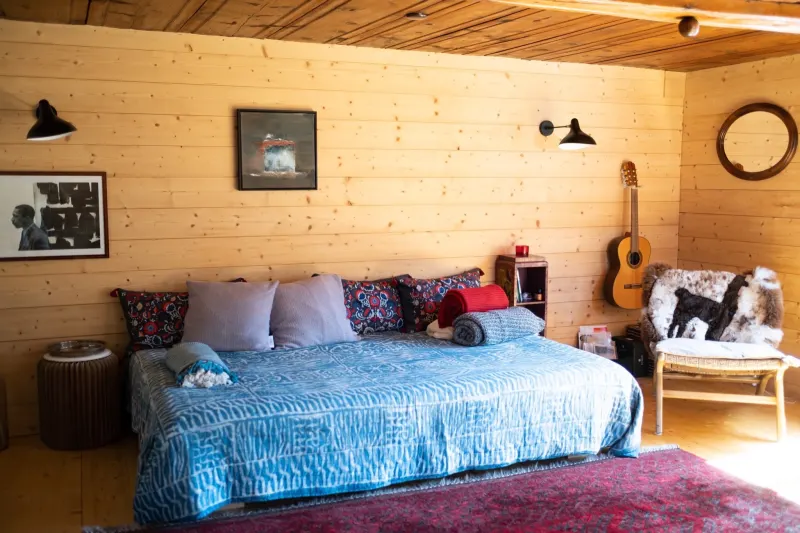 Chambre avec lit double, couvre-lit bleu et murs en bois clair